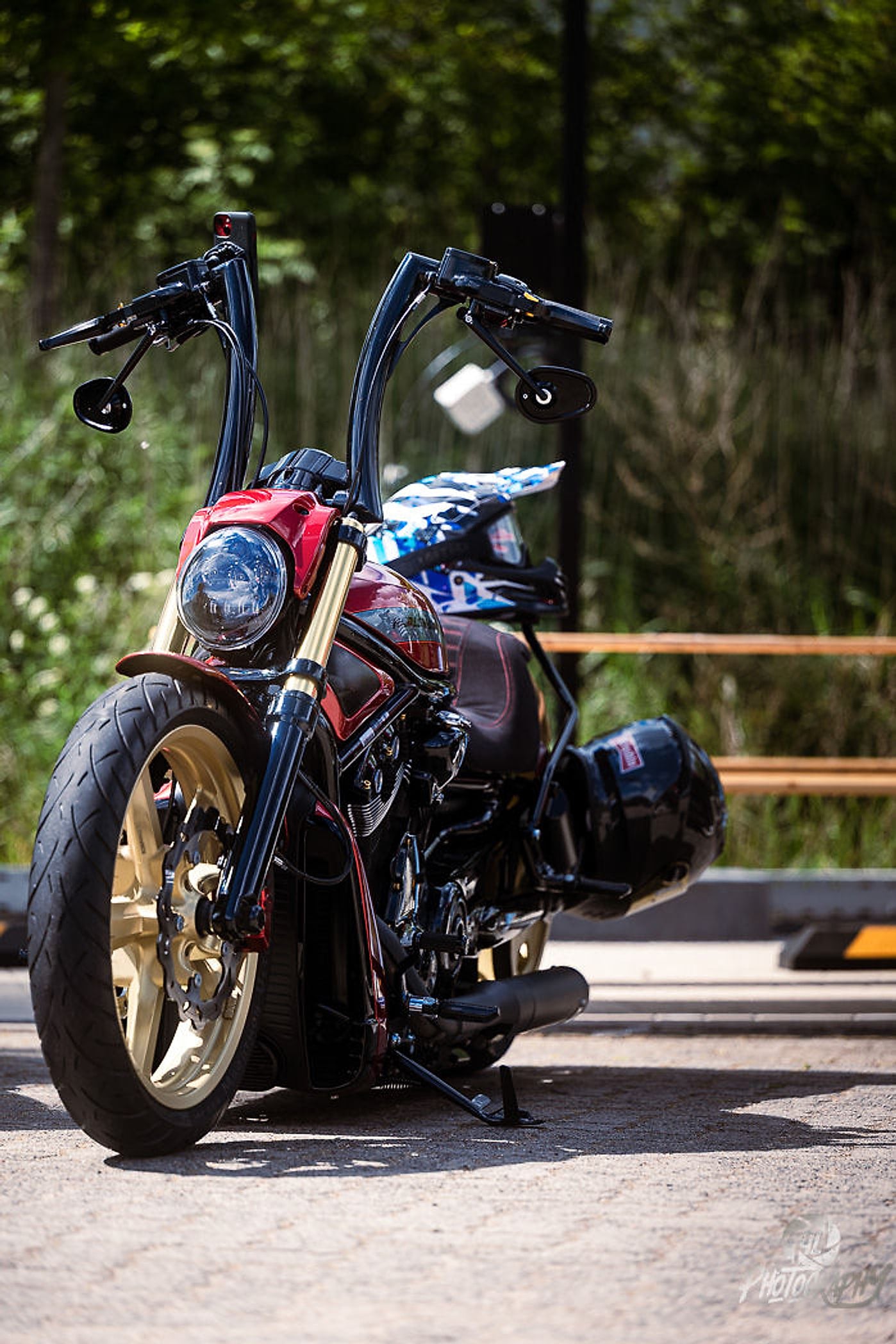 Custom Bike mit goldenen Felgen und hohem Lenker vor grünen Bäumen