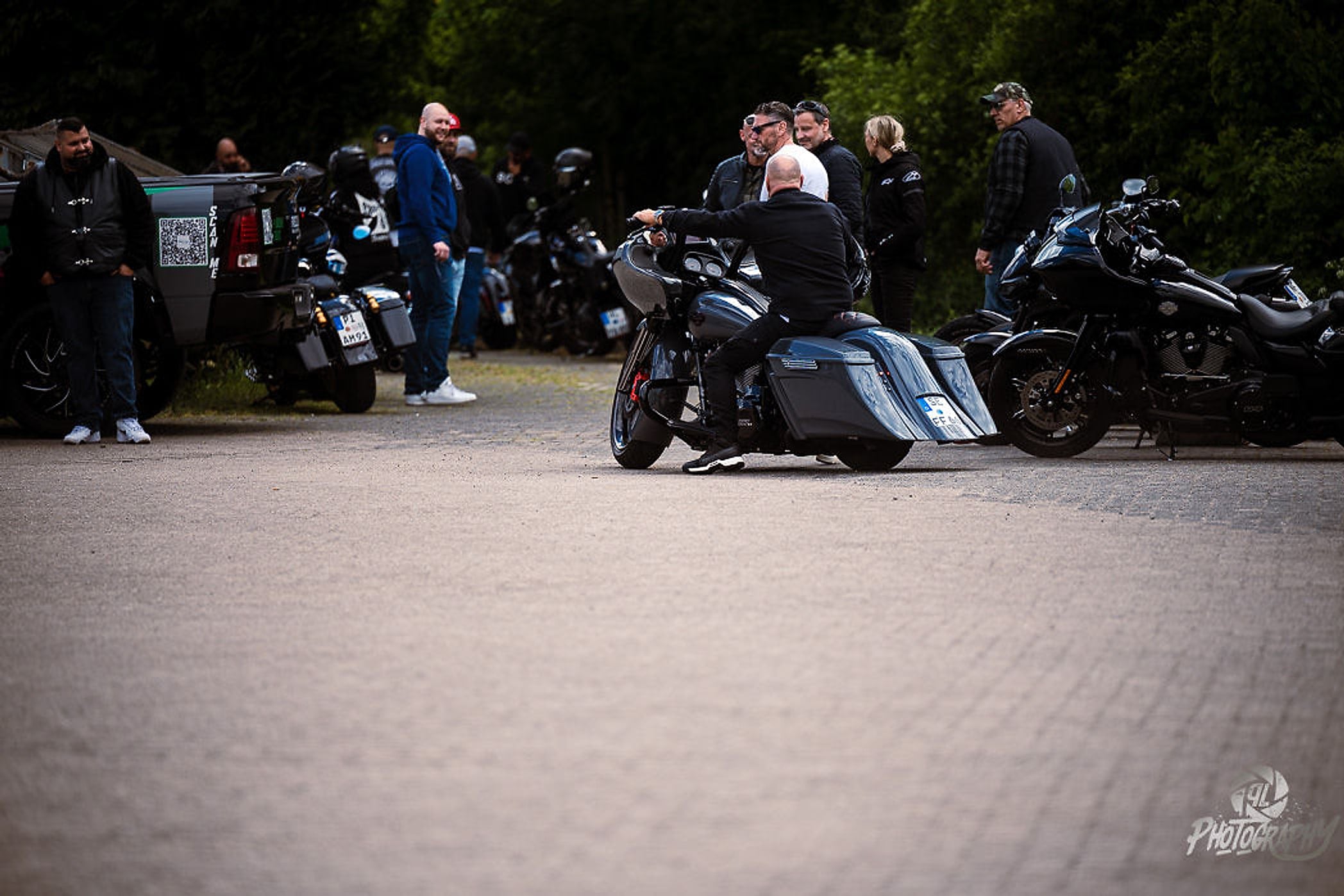 Biker auf grauem Bagger rollt über den Platz, Besucher am Rand