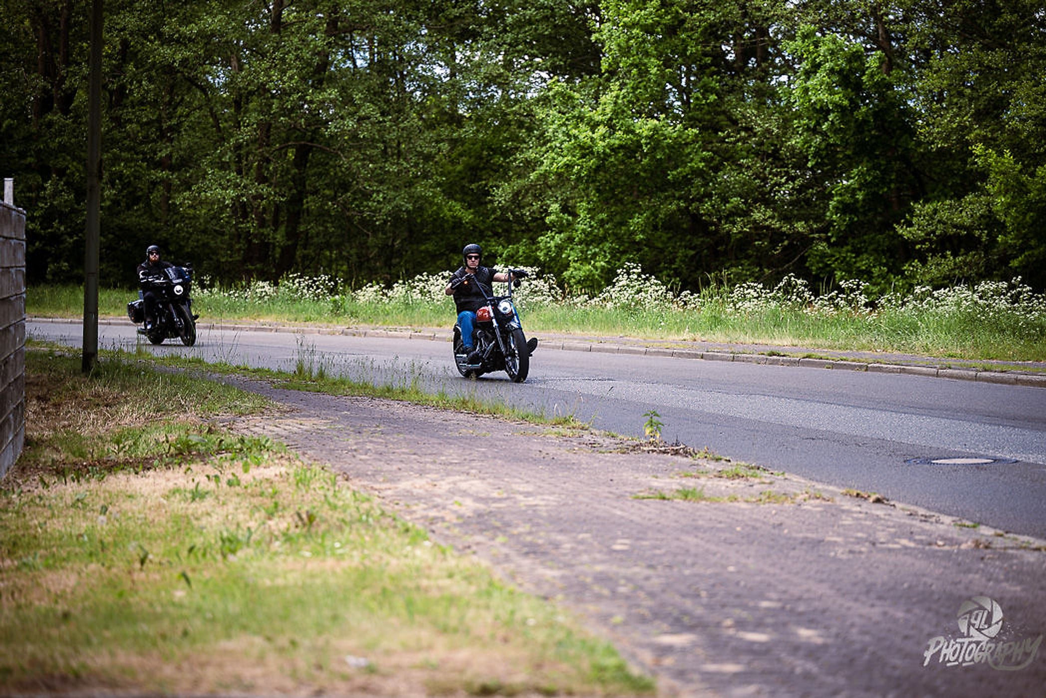 Zwei Motorräder fahren auf einer Landstraße zwischen Bäumen